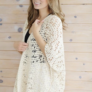 May include: A white crochet cardigan with a lacy openwork design. The cardigan has a relaxed fit and a slightly longer back hem.