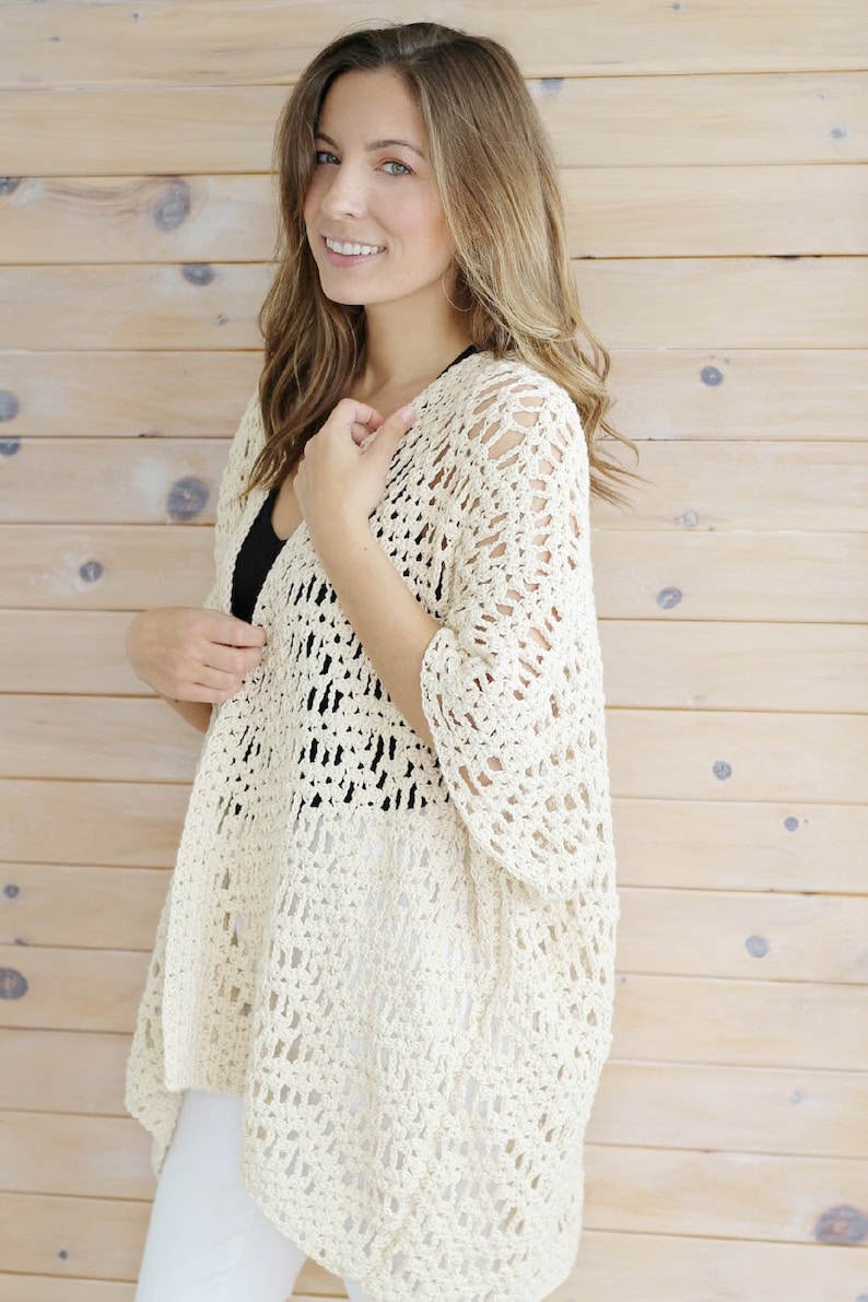 May include: A white crochet cardigan with a lacy openwork design. The cardigan has a relaxed fit and a slightly longer back hem.