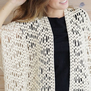 May include: A crocheted off-white cardigan with a lacy pattern. The cardigan has short sleeves and an open front.