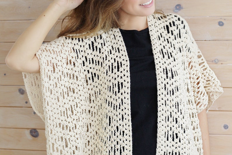 May include: A crocheted off-white cardigan with a lacy pattern. The cardigan has short sleeves and an open front.
