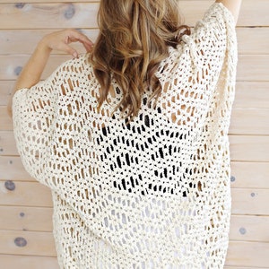 May include: A crocheted off-white cardigan with a loose, open-weave design. The cardigan has a relaxed fit and a slightly cropped length.