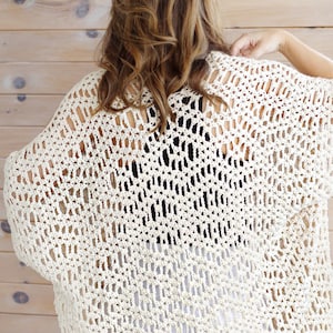 May include: A crocheted cream-colored cardigan with a loose, open-weave design. The cardigan is shown from the back and has a slightly cropped length.
