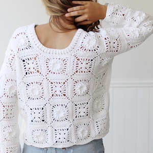 May include: White crochet sweater with a loose fit and a square pattern. The sweater has a round neckline and long sleeves.