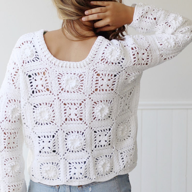 May include: White crochet sweater with a loose fit and a square pattern. The sweater has a round neckline and long sleeves.