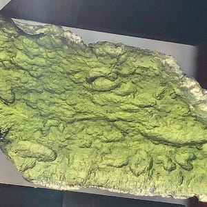 May include: A large, green, irregularly shaped piece of moldavite, a type of tektite, with a rough, textured surface.