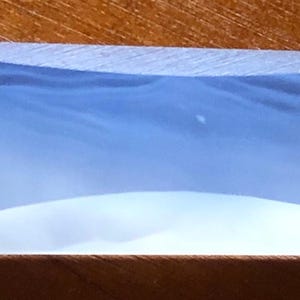 May include: A clear, rectangular, slightly curved glass lens with a frosted appearance.