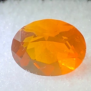 May include: A bright orange oval-shaped gemstone with a smooth, polished surface.