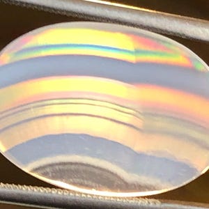 May include: A clear, oval-shaped agate gemstone with iridescent bands of yellow, orange, red, blue, and green.