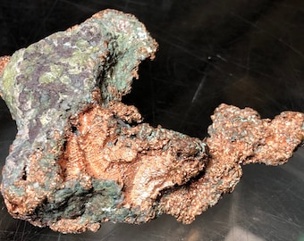 Könnte beinhalten: Ein großes, unregelmäßig geformtes Stück Kupfererz mit einer rauen, strukturierten Oberfläche. Das Kupfer ist rotbraun und hat an einigen Stellen eine grüne Patina.
