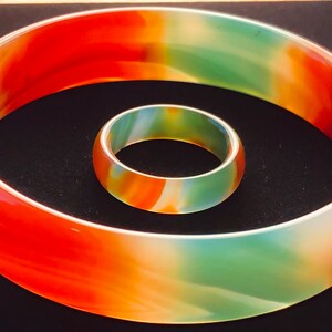 May include: Two agate bangles, one larger than the other, with a swirling pattern of green, orange, and white.