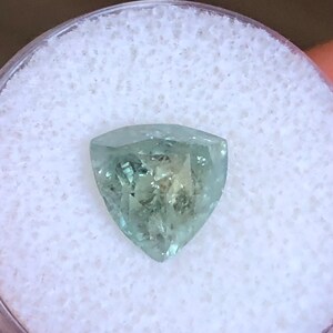 May include: A light green gemstone with a triangular shape, set in a white foam container.