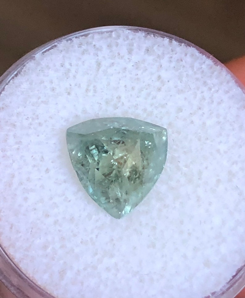 May include: A light green gemstone with a triangular shape, set in a white foam container.