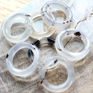 May include: Six white agate rings with black markings. The rings are stacked on top of each other and are on a wooden surface.