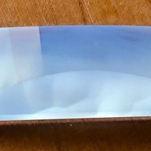 May include: A light blue, translucent, rectangular prism with a slightly curved surface. The prism has a white, opaque stripe running along the top.