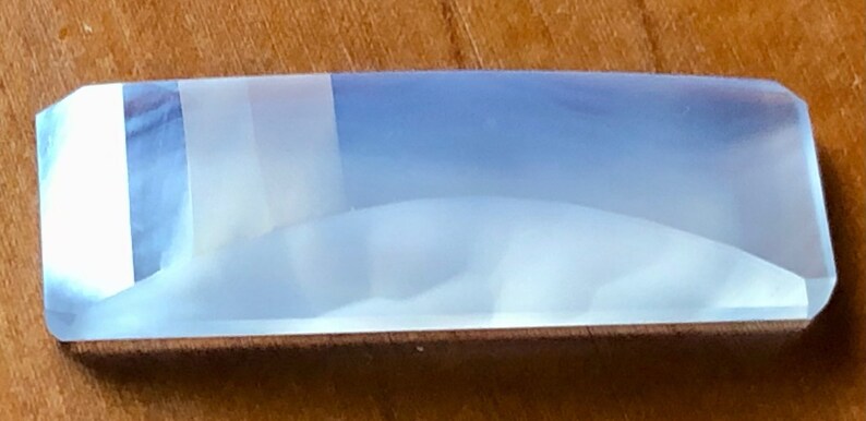 May include: A light blue, translucent, rectangular prism with a slightly curved surface. The prism has a white, opaque stripe running along the top.
