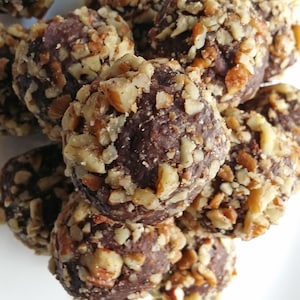 May include: A close-up of a pile of chocolate truffles covered in chopped pecans.
