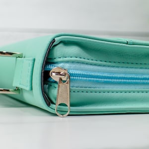 May include: A light blue zippered pouch with a silver zipper pull. The pouch has a strap on the side.