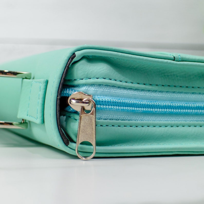 May include: A light blue zippered pouch with a silver zipper pull. The pouch has a strap on the side.