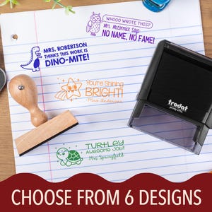 May include: A collection of six self-inking stamps with fun designs and phrases, including a dinosaur, owl, star, and turtle. The stamps are on lined paper, with a wooden stamp and a black stamp visible. The text "CHOOSE FROM 6 DESIGNS" is at the bottom.