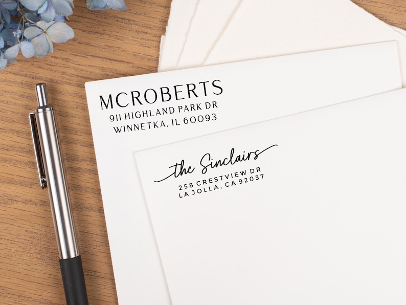 May include: White stationery with printed addresses for McRoberts and the Sinclairs. The McRoberts address is 911 Highland Park Dr, Winnetka, IL 60093. The Sinclairs address is 258 Crestview Dr, La Jolla, CA 92037. A silver pen rests on a wooden surface.