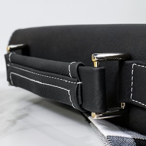 May include: Black leather carrying case with a white stitched handle and silver metal clasps.