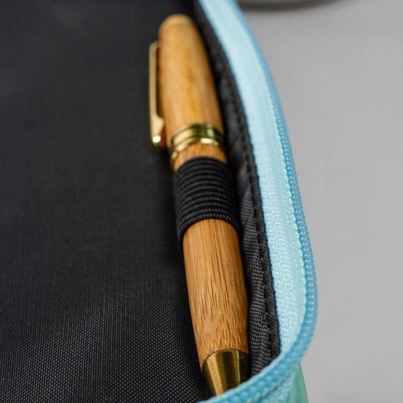 May include: A wooden pen with gold trim and black accents is partially inserted into a light blue zippered pouch.