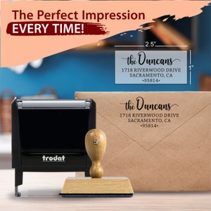 Self-inking and wood-handled stamp next to a stamped envelope in black ink with a return address on the flap. A sizing label shows that the stamped address is about 2.5" wide by 1" tall. The image states you'll get the perfect impression every time.