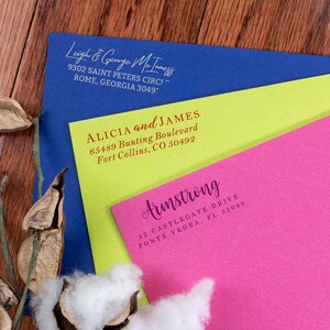 A navy, yellow, and pink envelope fanned out to show each envelope stamped in a different address design all stamped in different ink colors. The blue envelope stamped in silver ink, the yellow stamped in red ink, and the pink stamped in purple ink.