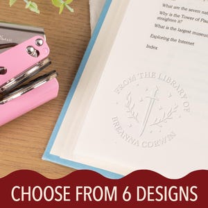 May include: A pink Model-ES book embosser next to a book with a custom library stamp. The stamp reads "From the Library of Breanna Corwin" with a sword and laurel wreath design. The image also includes the text "CHOOSE FROM 6 DESIGNS".