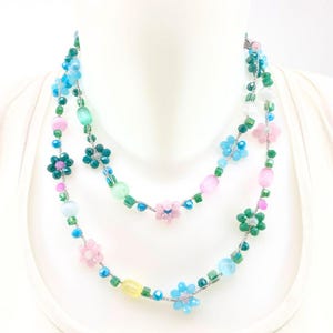 Peut inclure: Un collier à deux rangs avec un motif floral. Le collier est orné de perles roses, bleues, vertes et jaunes, avec de petits accents floraux. Le collier est présenté sur un mannequin blanc. Longueur approximative : 40 cm.