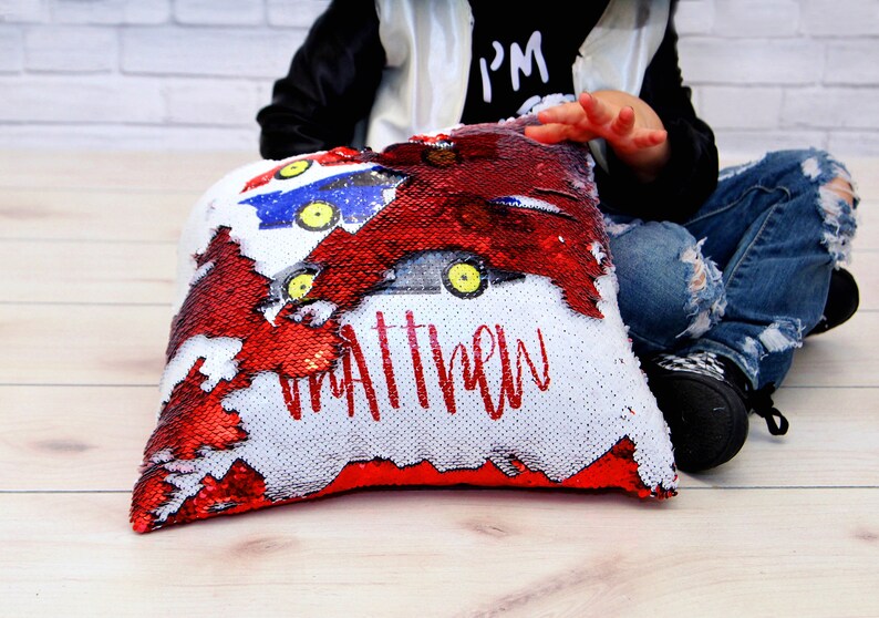 May include: A red and white reversible sequin pillow with a personalized name "Matthew" and a design of cartoon race cars.