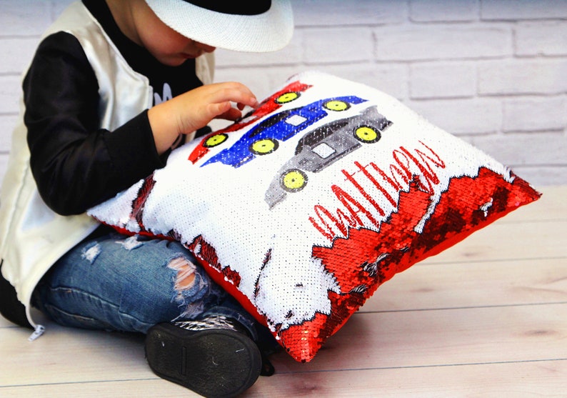 May include: A white and red reversible sequin pillow with a blue, red, and black car design and the name "Matthew" written in black.