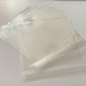 Peut inclure: Une pile de pochettes en plastique transparent et transparent. Les pochettes sont rectangulaires et semblent être scellées sur trois côtés, le quatrième côté étant ouvert. Le plastique est fin et souple, et les pochettes sont empilées les unes sur les autres.
