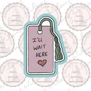 May include: A pink tag-shaped cookie cutter with the words "I'LL WAIT HERE" and a heart. The tag has a teal outline, a green tassel, and a loop at the top. The design is whimsical and suitable for baking.