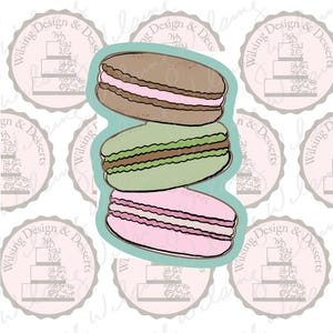 May include: A stack of three macarons, one brown, one green, and one pink, with a light brown filling. The macarons are on a light blue background.