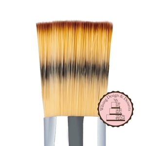 May include: A close-up of a flat, angled brush with a silver handle. The brush has a two-toned bristle design with brown and beige bristles. The brush is designed for cake decorating and is a product of Wilsing Design & Desserts.