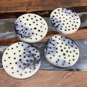 May include: Four round coasters with a white background and black polka dots. The coasters have a blue and white marbled design.