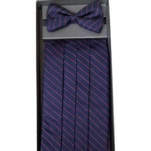 May include: A navy blue bow tie and cummerbund set with thin red stripes, presented in a black box. The bow tie is pre-tied. The cummerbund is pleated and features the same striped pattern. A formal accessory set.