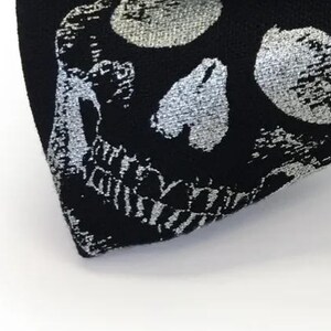 May include: A black bow tie featuring a repeating pattern of silver skulls. The bow tie is a classic accessory, suitable for formal events or adding a unique touch to an outfit. The skulls are detailed and add a gothic flair.