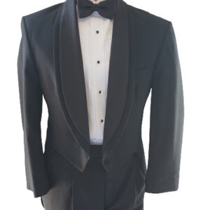 May include: A black tuxedo with a satin shawl collar and matching pants. The jacket has a single button closure and the pants have a pleat in the front.
