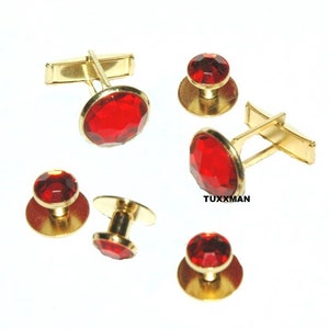 May include: A set of red and gold cufflinks and studs. The cufflinks have a round red stone in the center and the studs have a smaller round red stone. The text "TUXXMAN" is visible in the image.