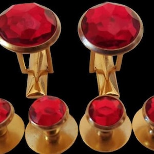 May include: A set of four gold cufflinks and studs with red glass stones. The cufflinks have a rounded shape and the studs are round.