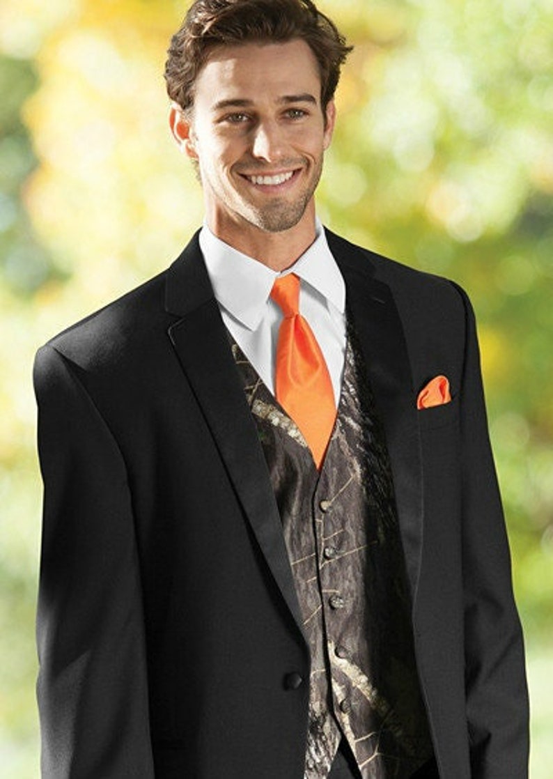 Puede incluir: Una chaqueta de traje negra con un chaleco de camuflaje y una corbata naranja. La chaqueta tiene una solapa de sat&eacute;n y un pa&ntilde;uelo de bolsillo.