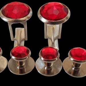 May include: A set of red crystal cufflinks and shirt studs. The cufflinks have a silver-toned metal base and the studs have a silver-toned metal base with a round, silver-toned metal back.