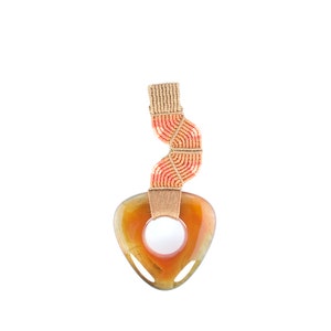 May include: A heart-shaped pendant made of orange agate with a hole in the center. The pendant is attached to a beige and orange macrame cord.