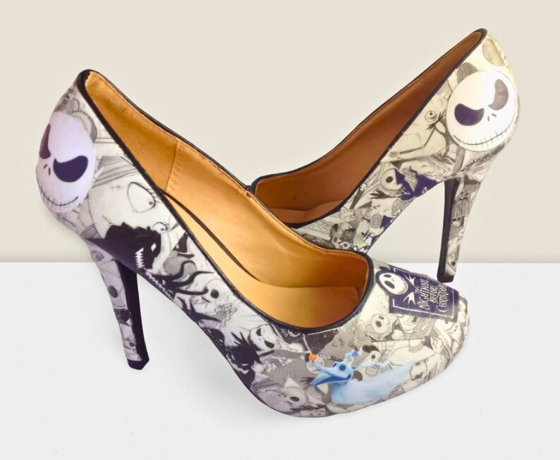 Puede incluir: Un par de zapatos de tac&oacute;n alto negros con un estampado blanco y negro con personajes de la pel&iacute;cula "Pesadilla antes de Navidad".