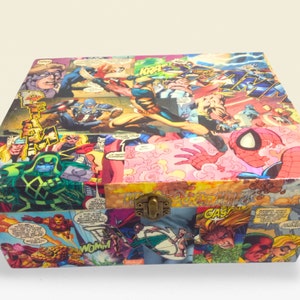 May include: A wooden box covered in a colourful collage of comic book pages featuring various superheroes, including Spider-Man, Wolverine, and Captain America. The box has a metal latch and is ideal for storing small items.