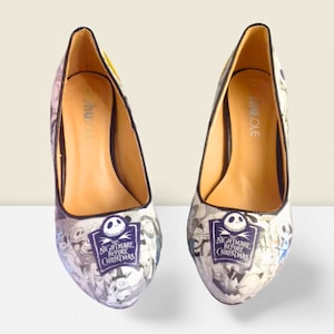 Puede incluir: Un par de zapatos de tac&oacute;n alto negros con un estampado blanco y negro con personajes de la pel&iacute;cula "Pesadilla antes de Navidad". Los zapatos tienen un tac&oacute;n negro y una puntera negra.