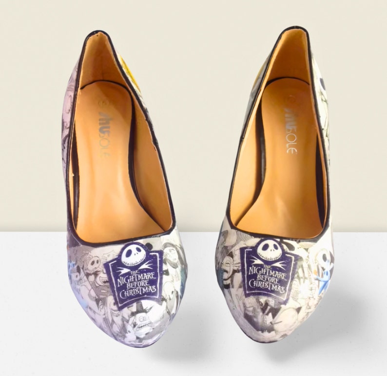 Puede incluir: Un par de zapatos de tac&oacute;n alto negros con un estampado blanco y negro con personajes de la pel&iacute;cula "Pesadilla antes de Navidad". Los zapatos tienen un tac&oacute;n negro y una puntera negra.