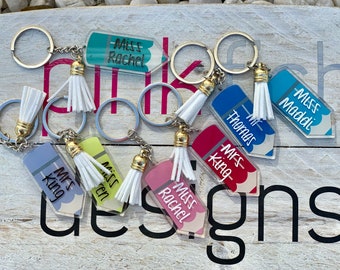 May include: A set of six colorful pencil-shaped keychains with white tassels. Each keychain features a teacher's name, including "Miss Rachel", "Mr Thomas", "Mrs King", "Miss Maddi", "Mrs King", and "Miss Wren".